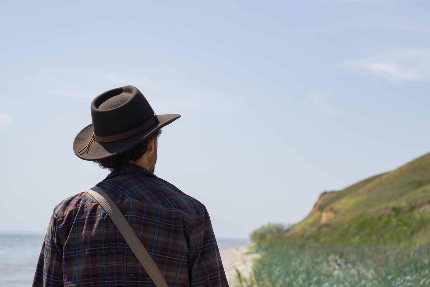 Back view of young male hiker in cowboy hat walking outdoors in summer day. Hipster traveler. photo