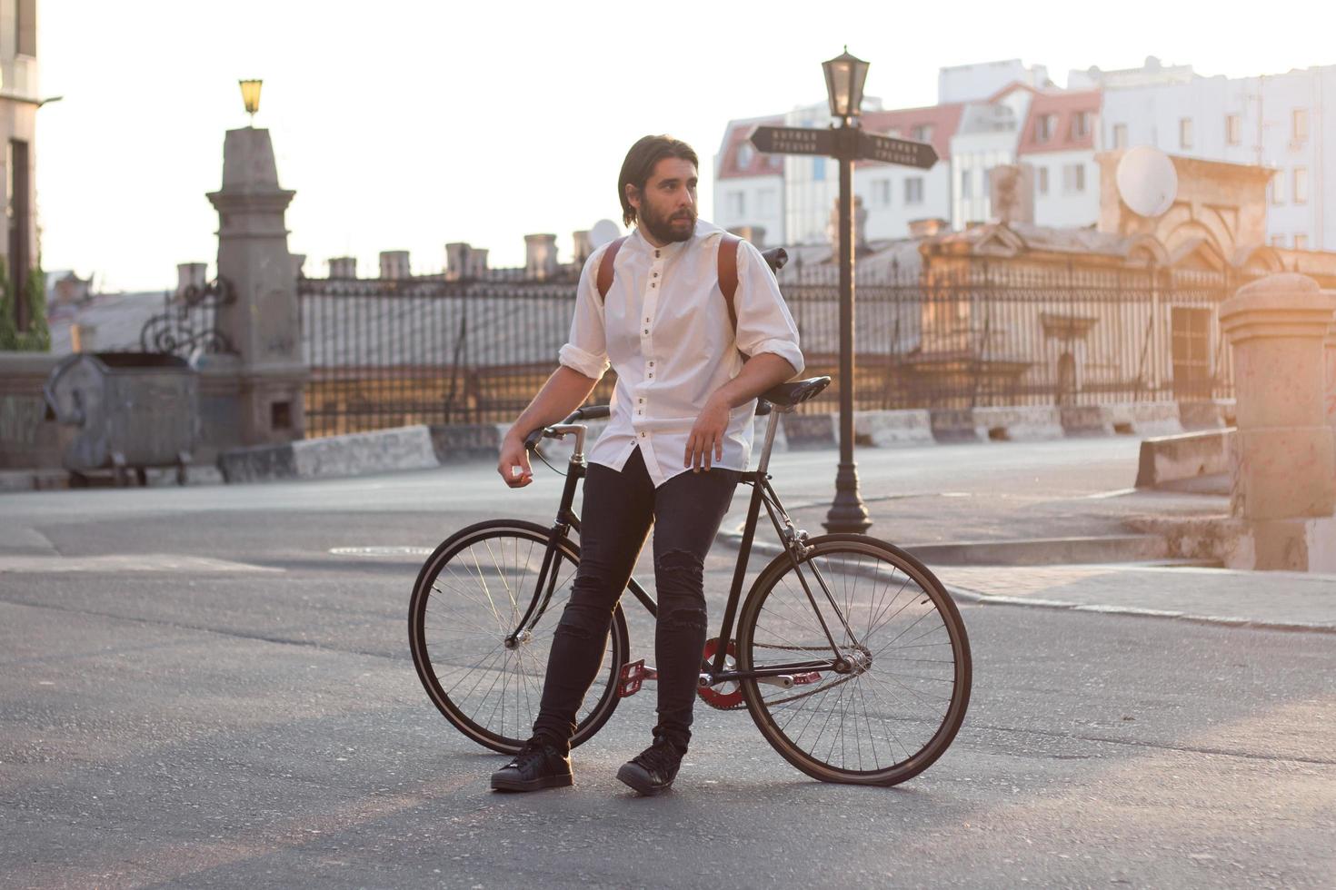 Young bearded man with leather backpack walking with black bicycle photo