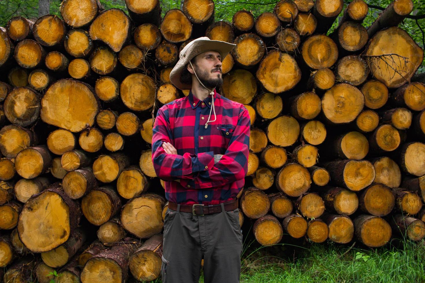 retrato de leñador en el bosque, muchos grandes troncos de pino en el fondo. joven excursionista masculino posando cerca de la harina de aserrín en el bosque de pinos. foto