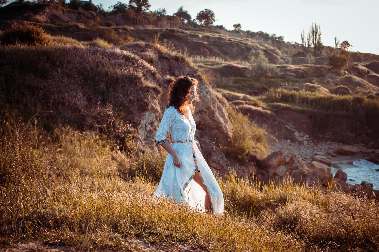 young woman walking on the morning beach in beautiful white dress. Fit female having good time during turing the sunrise. photo