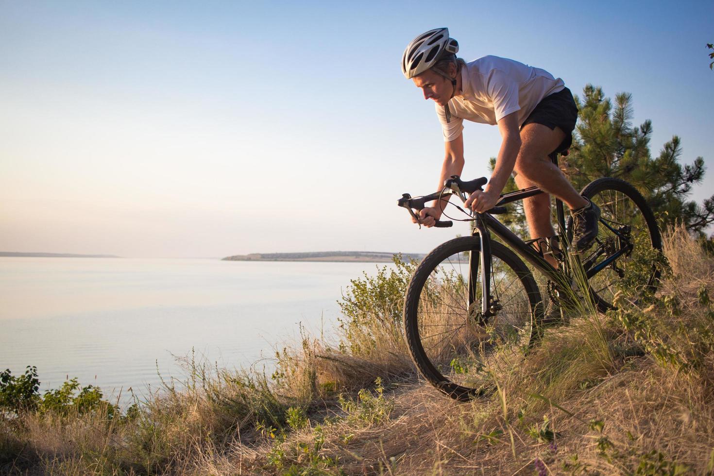 ciclista en bicicleta ciclocross profesional cuesta abajo, fondo de pino y lago foto