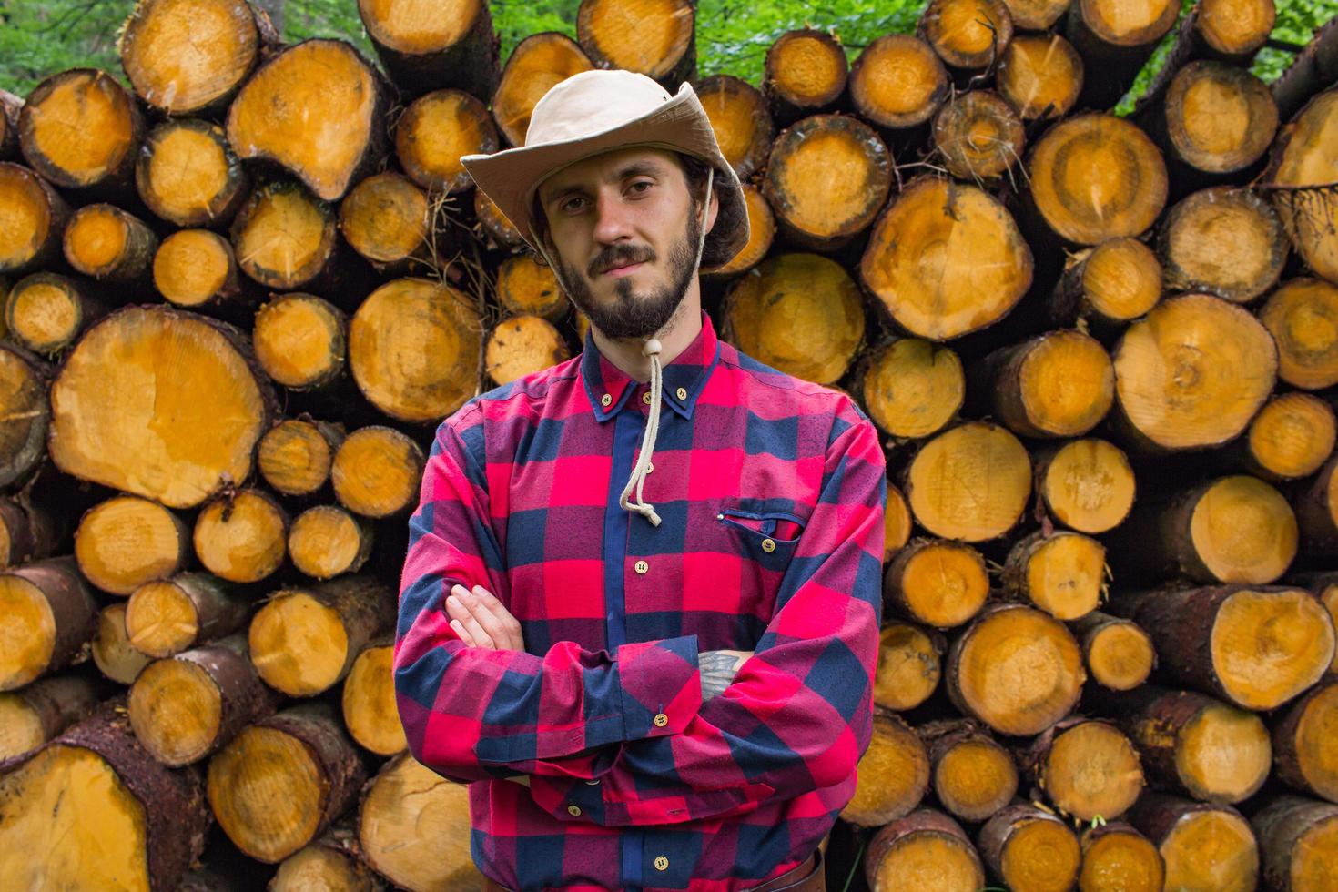 Portrait of lumberjack in forest, many big logs of pine on background. Young male hiker posing near the sawmeal in the pines forest. photo