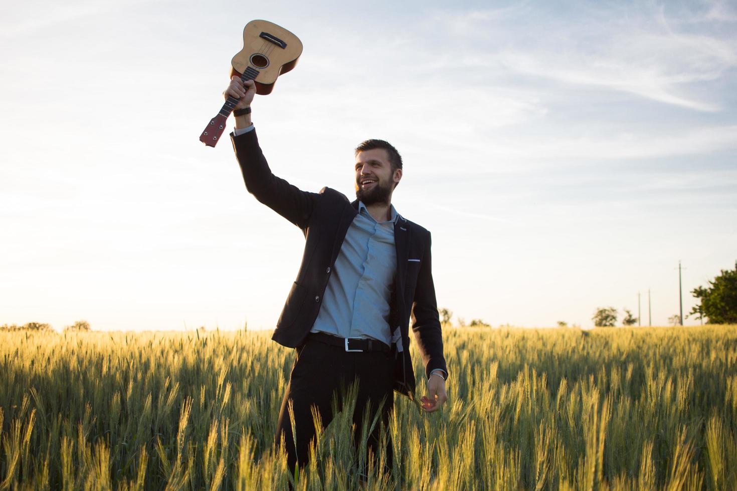 Happy manager with ukulele travel in summer wheat fields, buisinesman in suit play on ukulele, vacation or travel concept photo