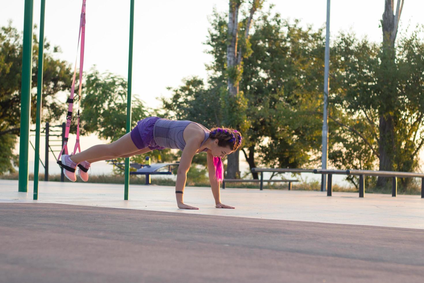 hermosa mujer en forma en ropa deportiva rosa y púrpura entrenando en el gimnasio al aire libre por la mañana, ejercicios con correas de suspensión en el parque foto
