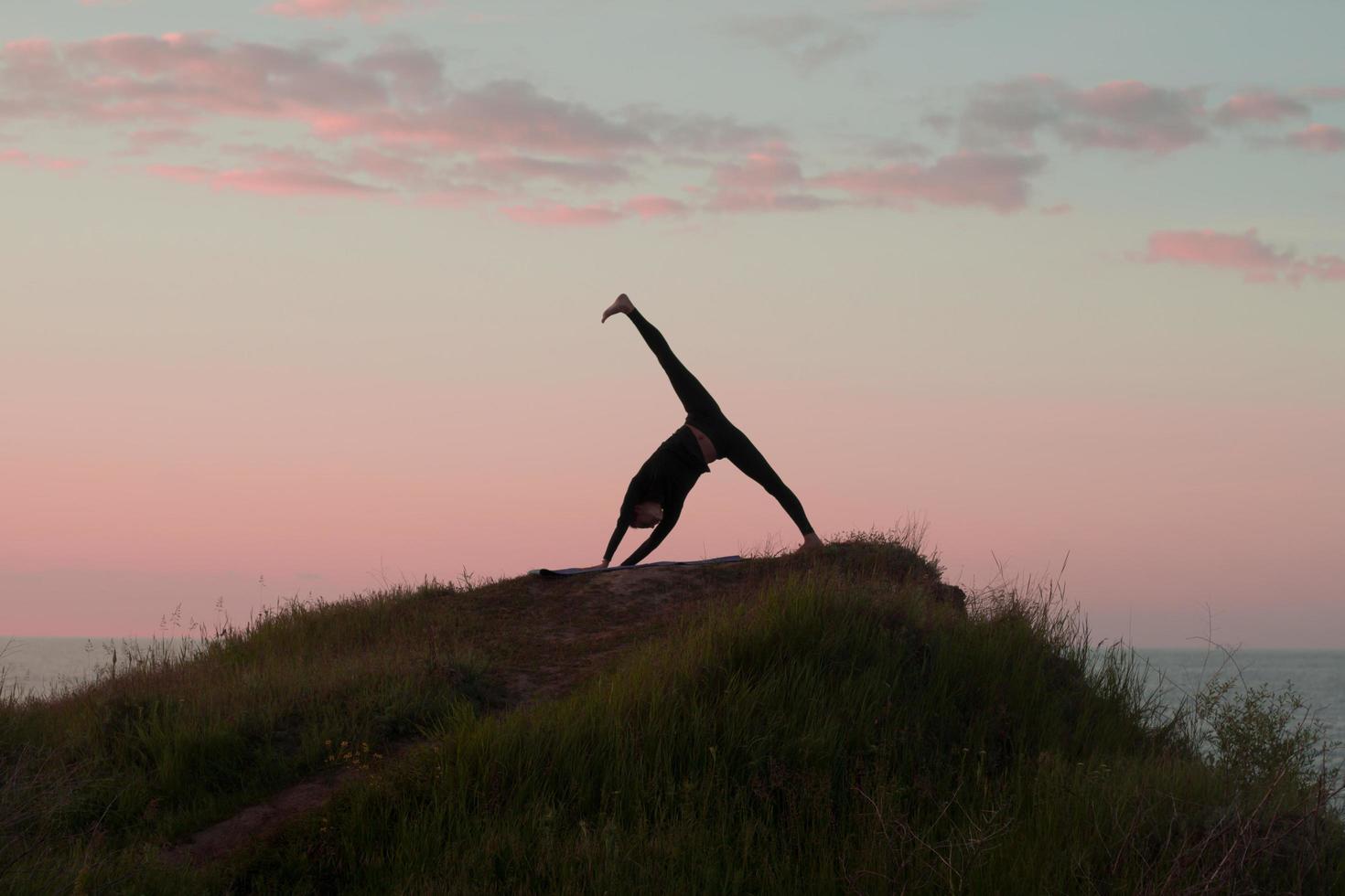 Fit woman doing yoga stretching exercise outdoor in beautiful mountains landscape. Female on the rock with sea and sunrise or sunset background training asans. Silhouette of woman in yoga poses photo