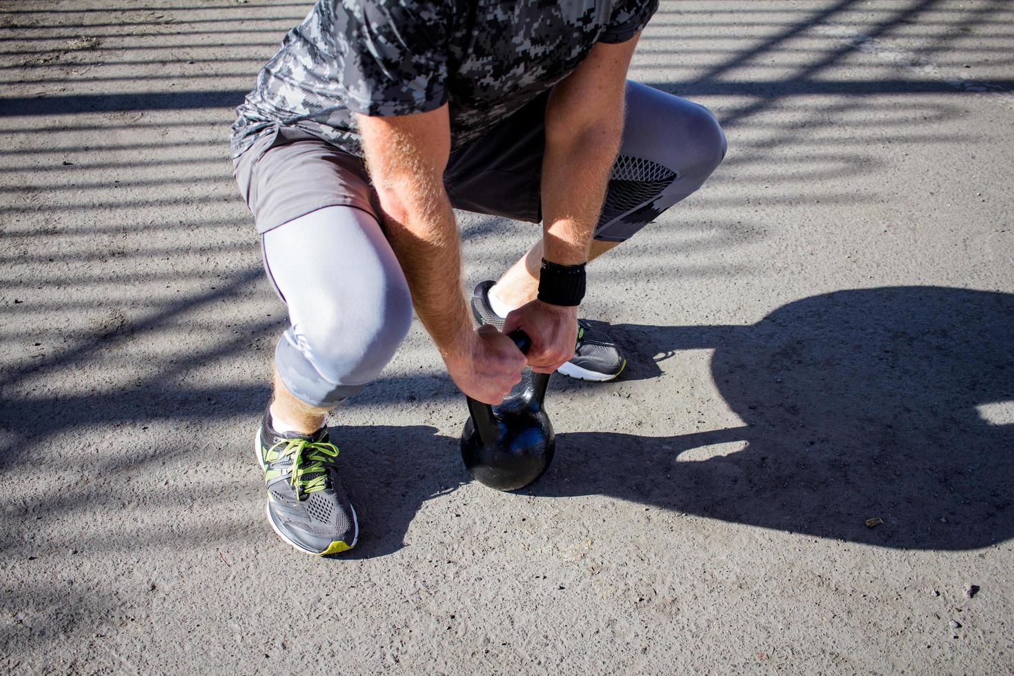 Young bearded male athlete training in industrial zone in sunny day, kettlebells exercises outdoors, urban background photo