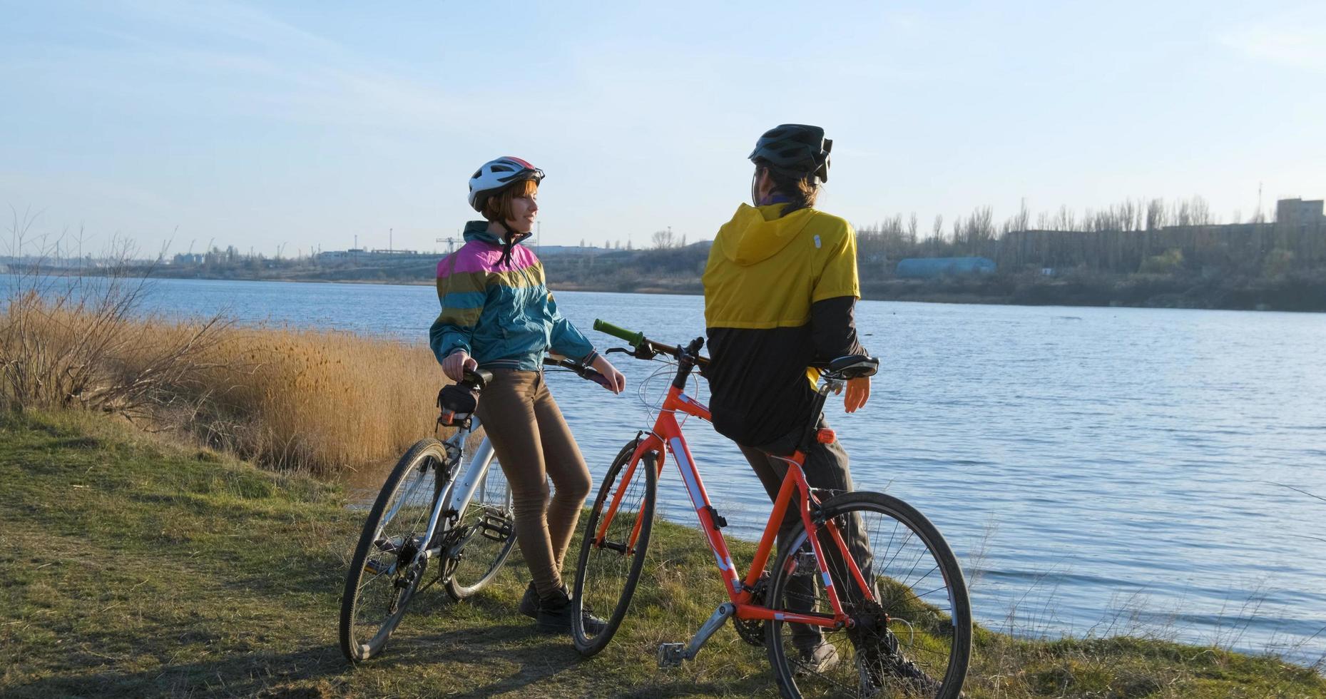 Couple of male and female ride on bicycles near river during sunset photo