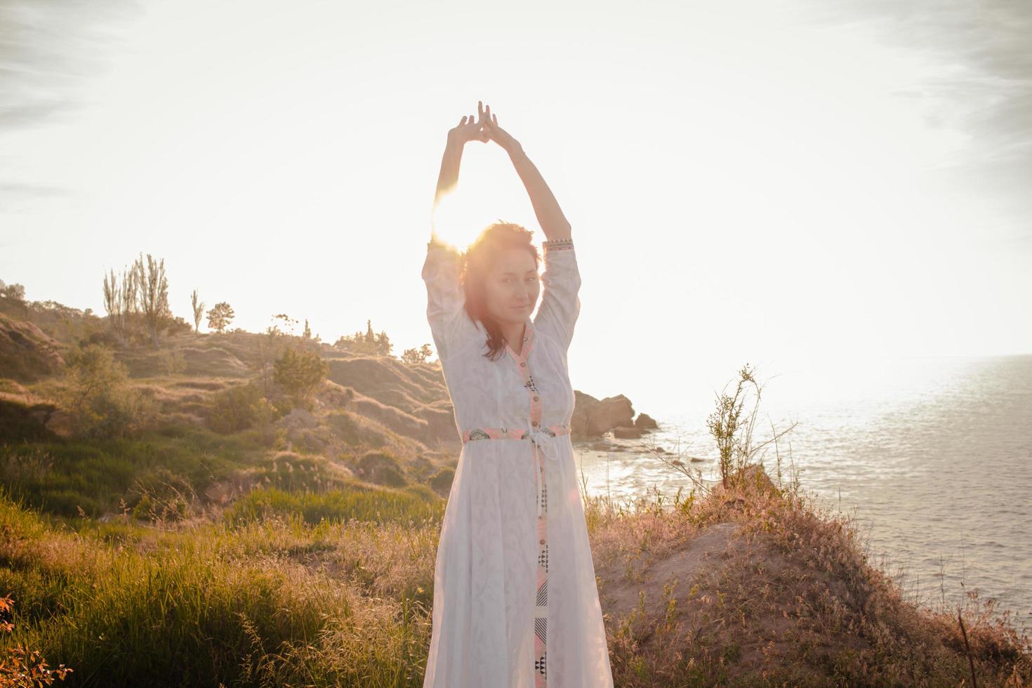 young woman walking on the morning beach in beautiful white dress. Fit female having good time during turing the sunrise. photo