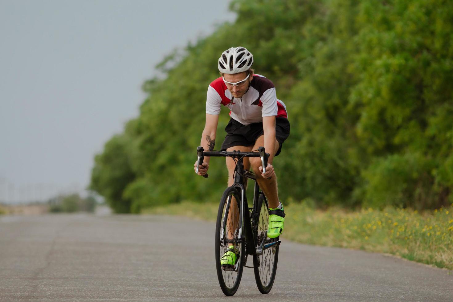 Bicycle racer in helmet and sportswear training alone on empty country road, fields and trees background photo