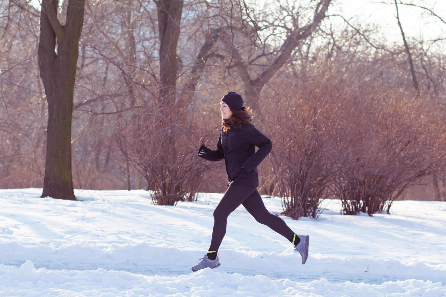 young woman athlete in black sport suit run in winter park photo