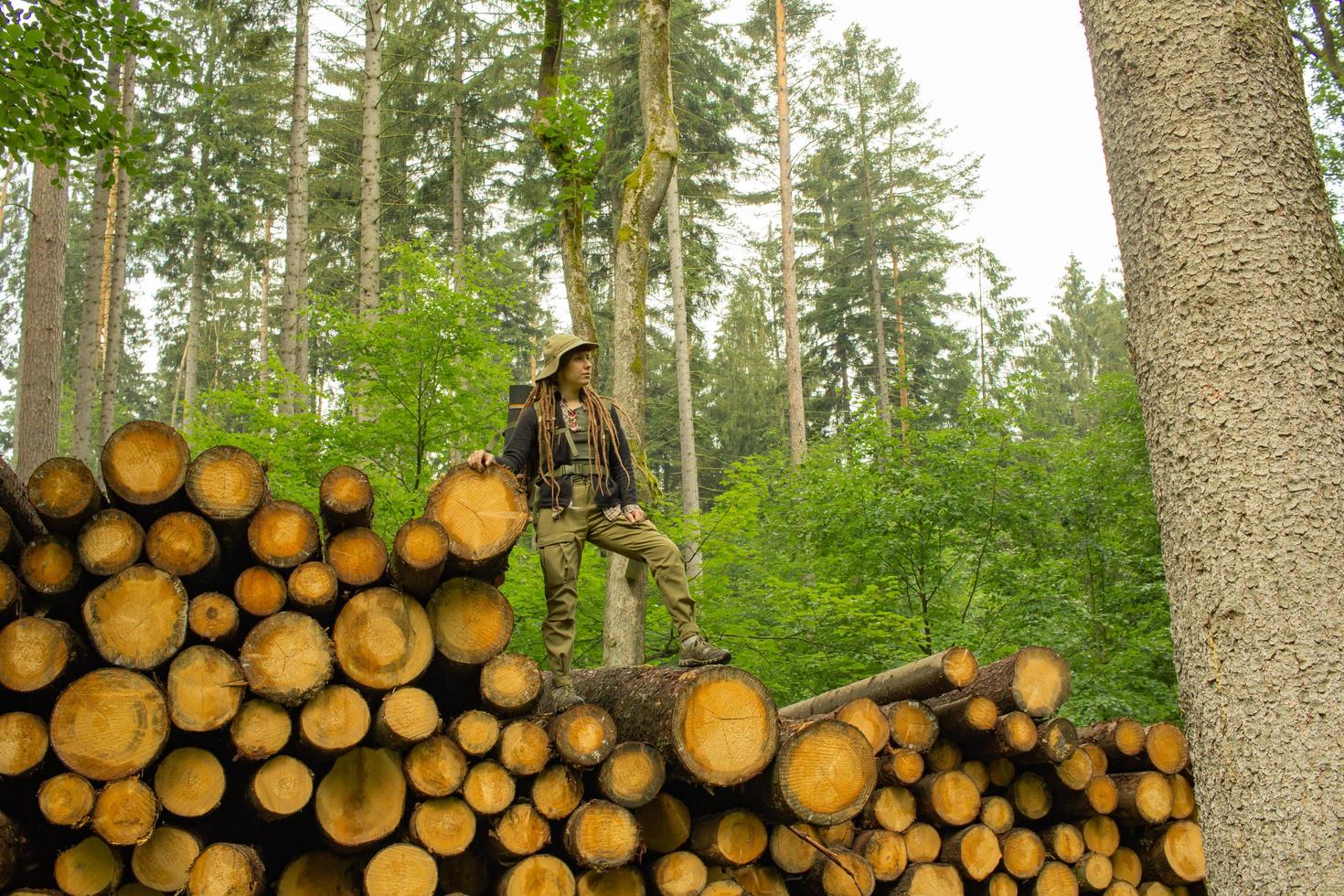 Young female hiker posing near the sawmeal in the pines forest. Many tree logs in the forest. Woman backpacker traveler. photo