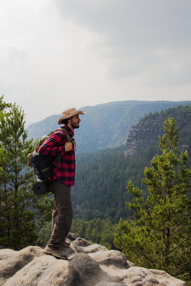 Young male hiker stand on the cliff in mountains with baclpack and hat photo