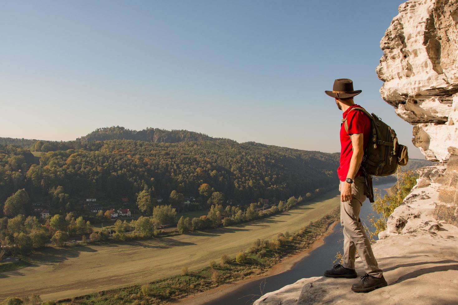 Young bearded male traveler in hat stand on the cliff in sunny day photo