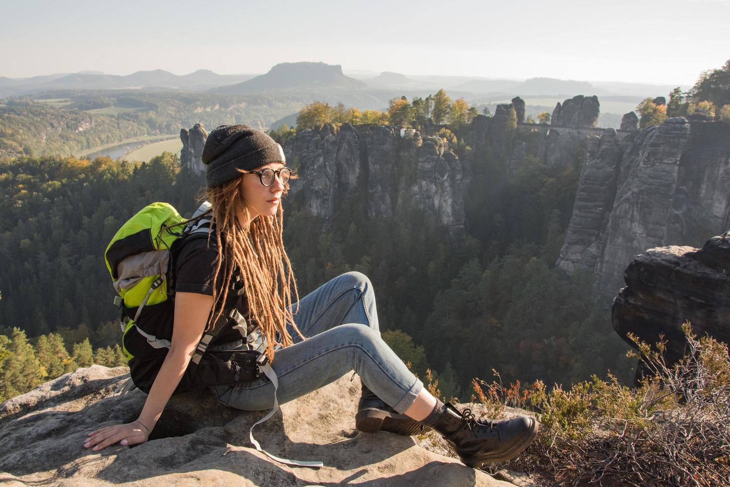 Young woman traveler with baclpack stand on the cliff in mountains photo