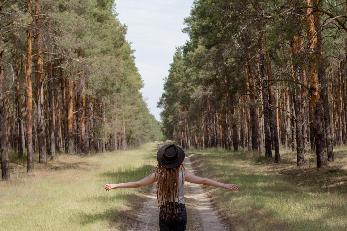 young woman with dreadlocks walking on the road, big pines background, girl hiker in woods photo