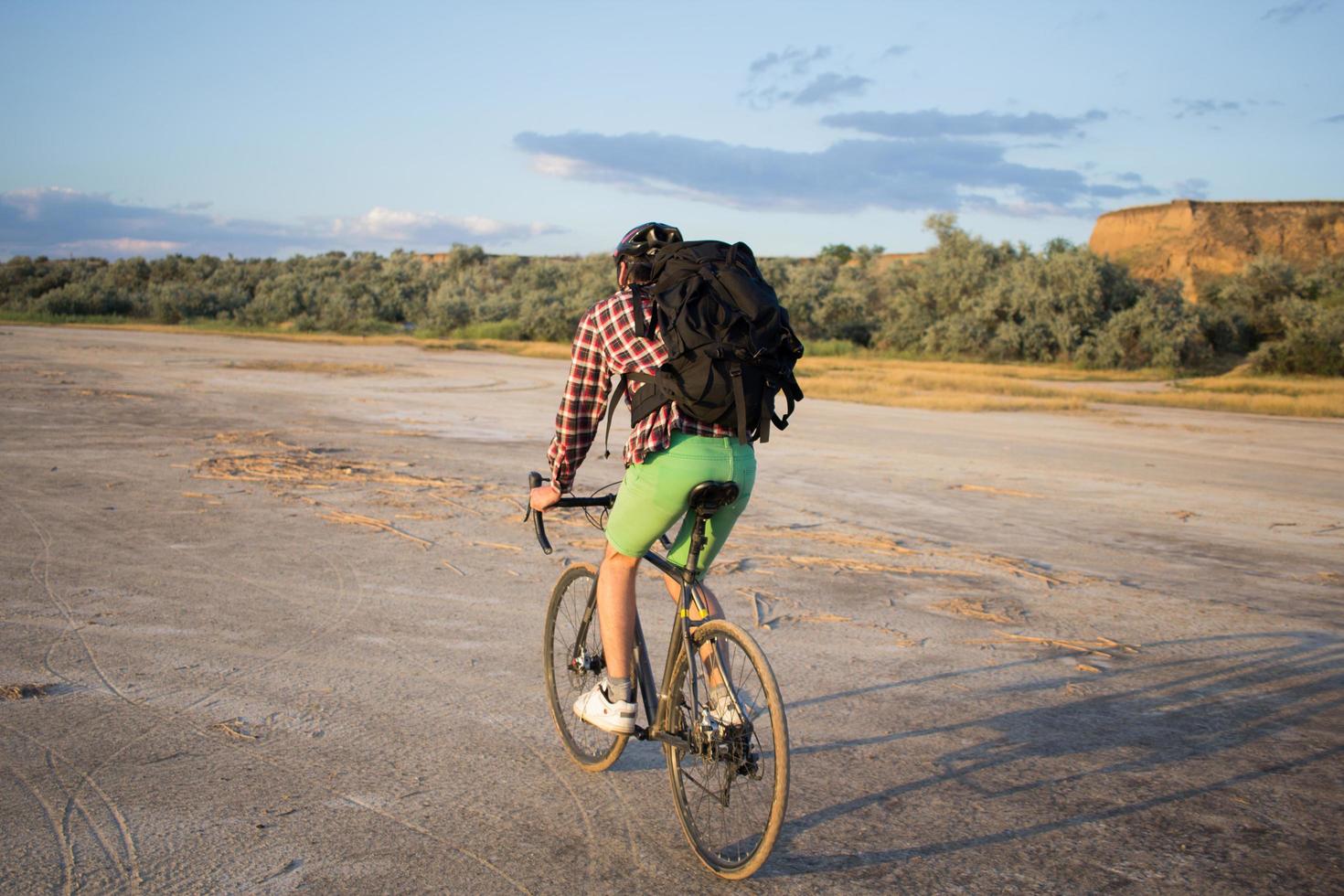 turista en bicicleta con mochilas y casco viaja en el desierto en su bicicleta de ciclocross durante la puesta de sol foto