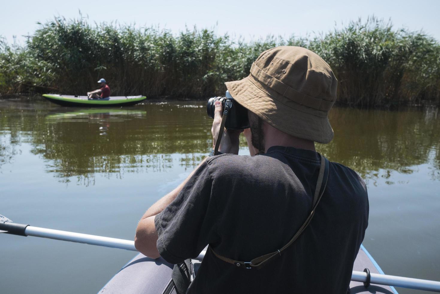 Young male traveler with photo camera swim on kayak in the river