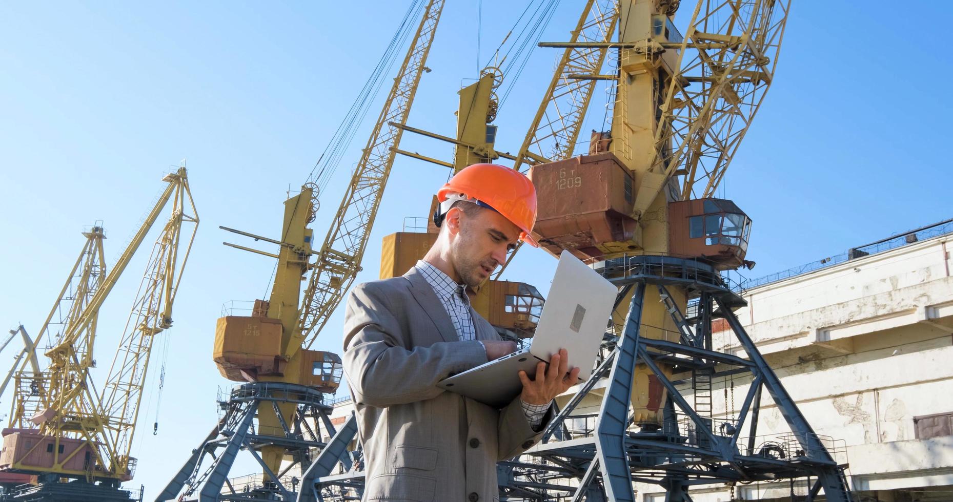 Young male worker of sea harbor in helmet, cargo manager in suit and halmet works outdoor , cranes and sea background photo