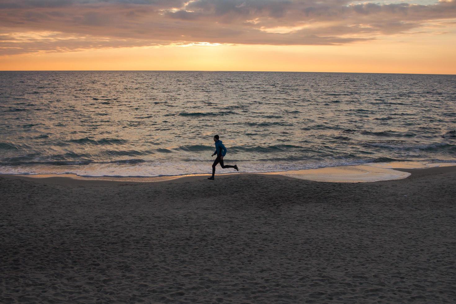 joven con ropa de otoño entrenando en la playa, fondo de amanecer, corredor masculino por la mañana foto