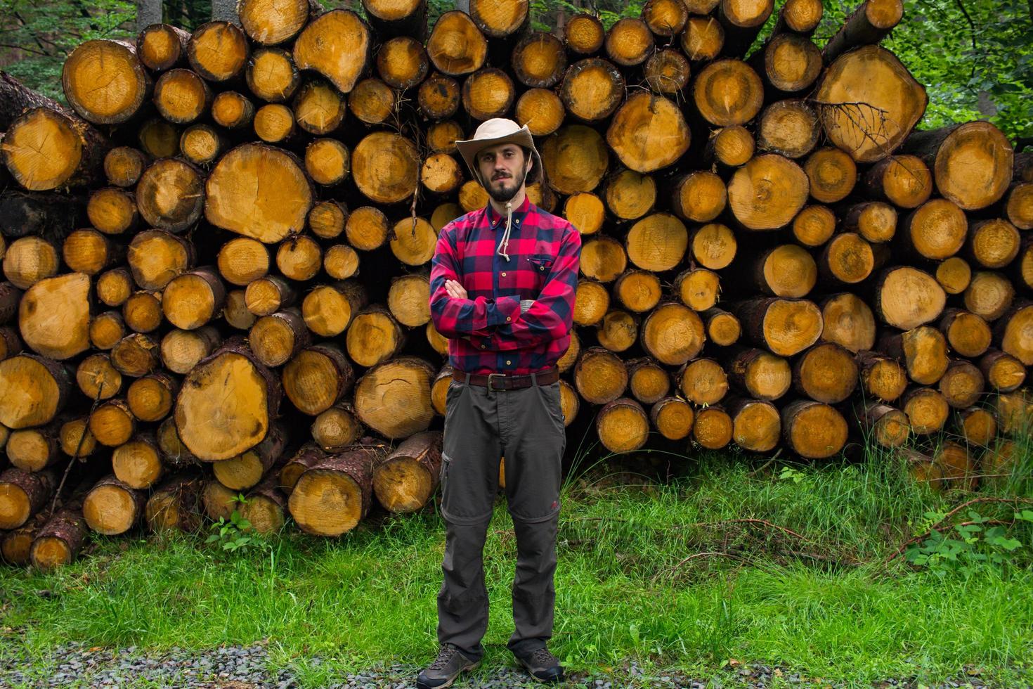Portrait of lumberjack in forest, many big logs of pine on background. Young male hiker posing near the sawmeal in the pines forest. photo