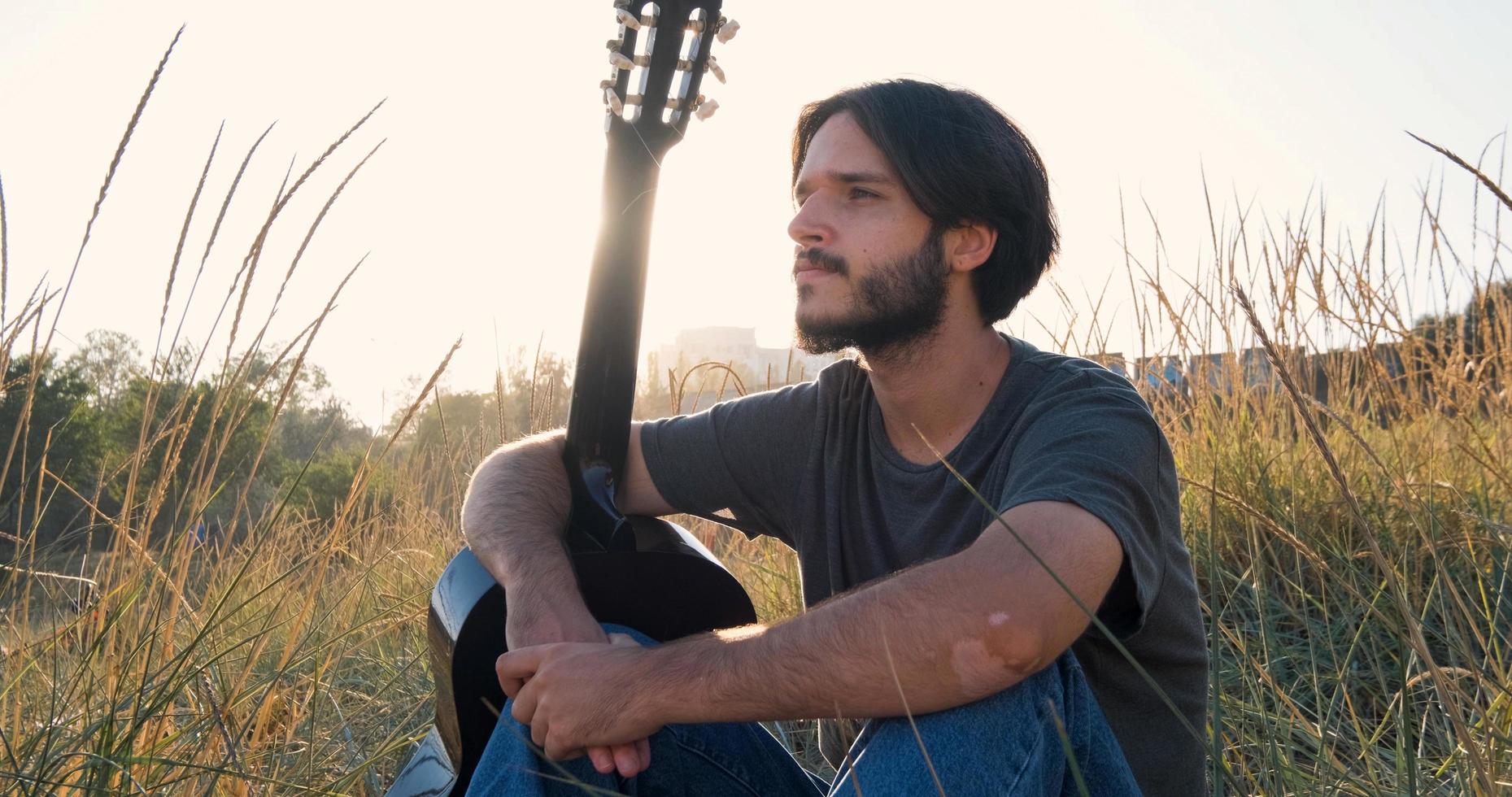 joven y apuesto hombre tocando guitarra acústica en la playa en un día soleado, mar u océano en el fondo foto