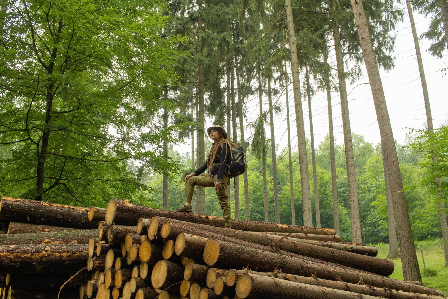 joven excursionista posando cerca de la harina de aserrín en el bosque de pinos. muchos troncos de árboles en el bosque. viajero mochilero mujer. foto