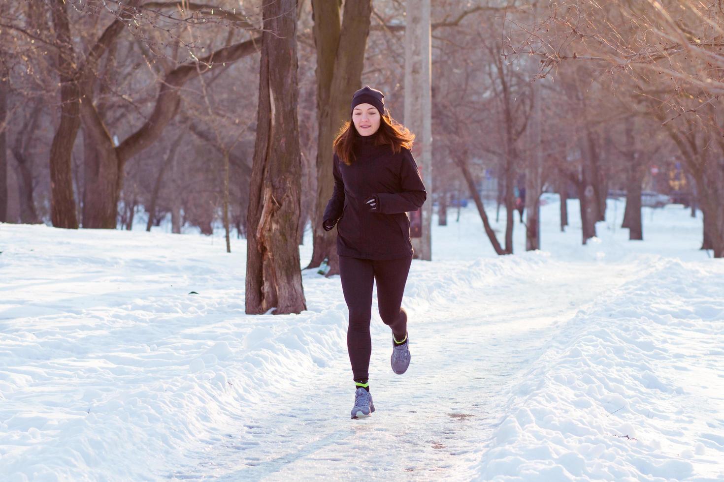 young woman athlete in black sport suit run in winter park photo