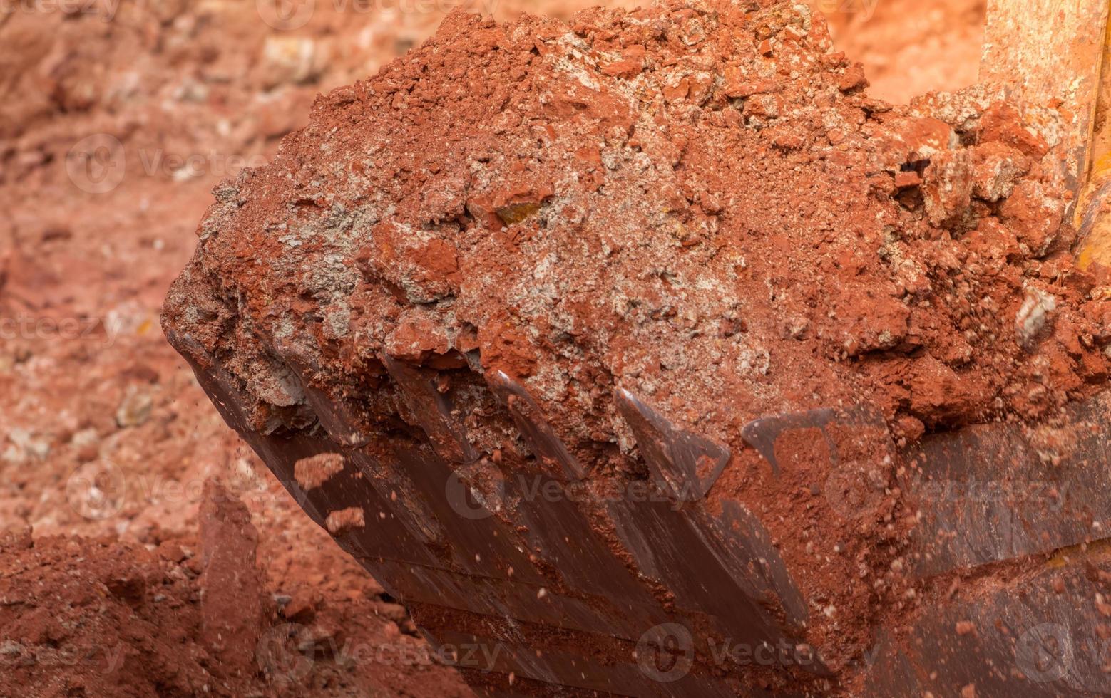 Backhoe working by digging soil at construction site. Bucket of backhoe digging soil. Crawler excavator full with orange and white soil. Excavating machine. Earth moving machine. Excavation vehicle. photo