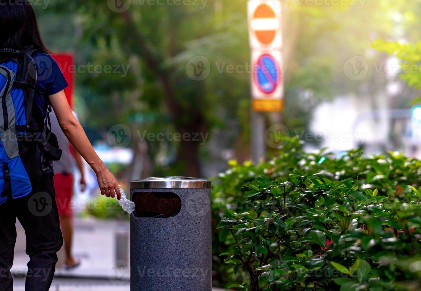 Woman hand throwing twisted empty water bottle in recycle bin. Gray plastic recycle bin. Backpacker discard bottle in trash bin. Waste management. Plastic bottle garbage. Reduce and reuse plastic. photo