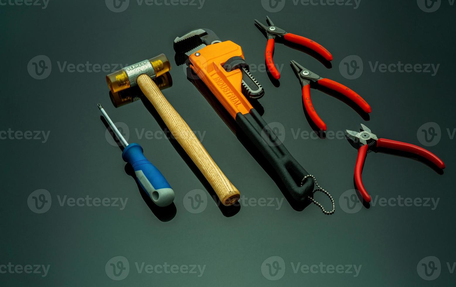 Set of mechanic tools isolated on black background. Screwdriver, red end cutter pliers, locking pliers, pincers, plastic hammer with wooden handle, and monkey pipe wrench. Tools for technician to fix. photo