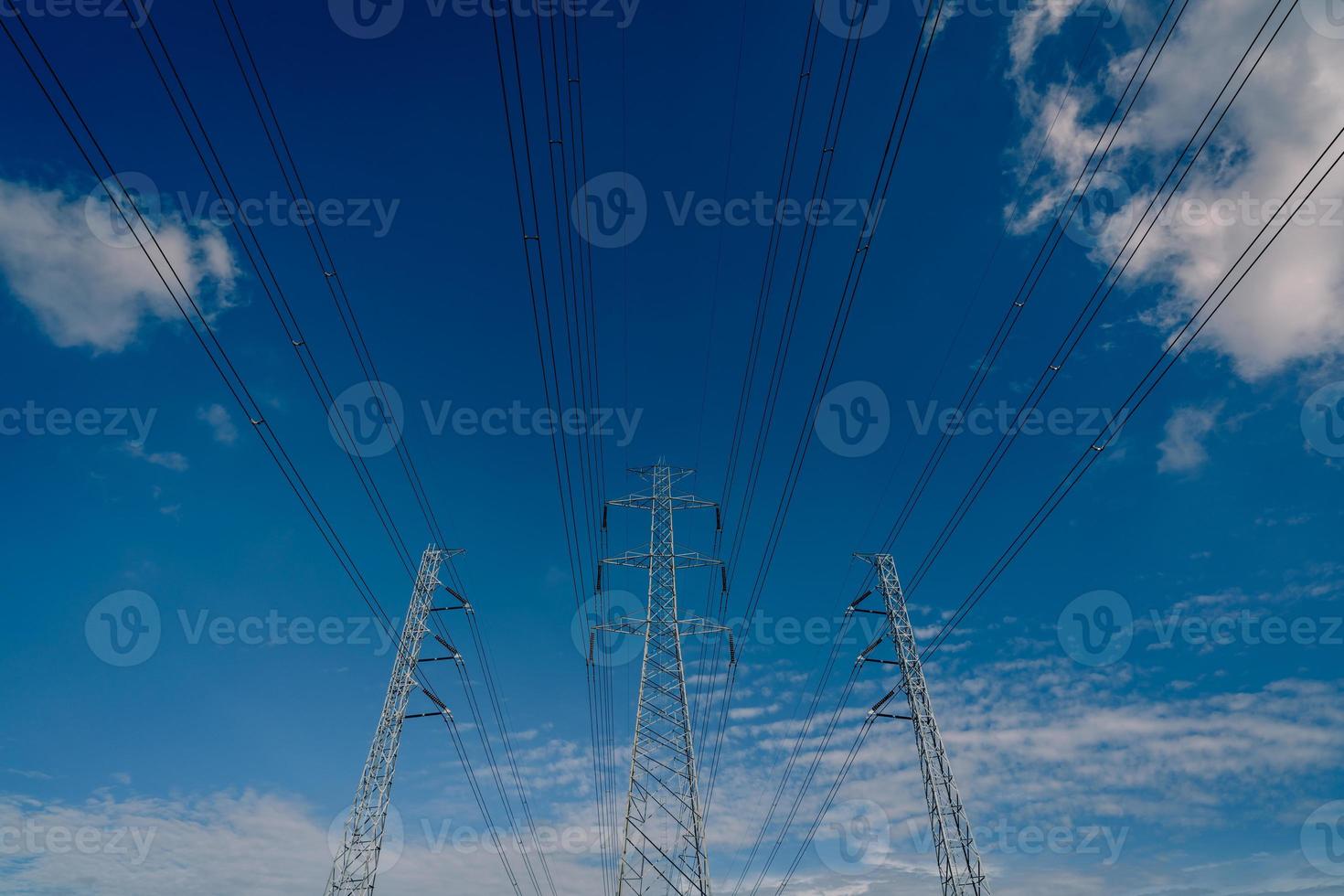 pilón eléctrico de alto voltaje y cable eléctrico contra el cielo azul y las nubes blancas. mirando hacia arriba la vista de la torre de electricidad. torre de red de alto voltaje con cable de alambre. concepto de potencia y energía. foto