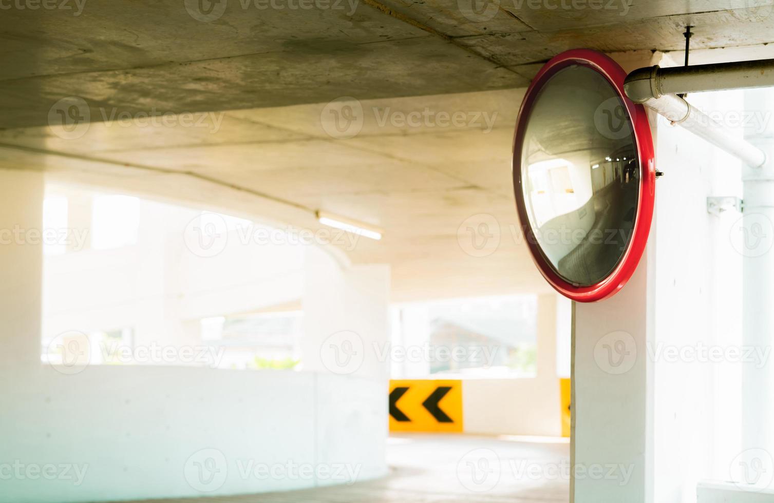 Convex safety mirror at curve of indoor car parking lot to reduce risk of accidents from blind corner or blind spots. Convex circular safety mirror in multi-level parking garage. Indoor traffic convex photo