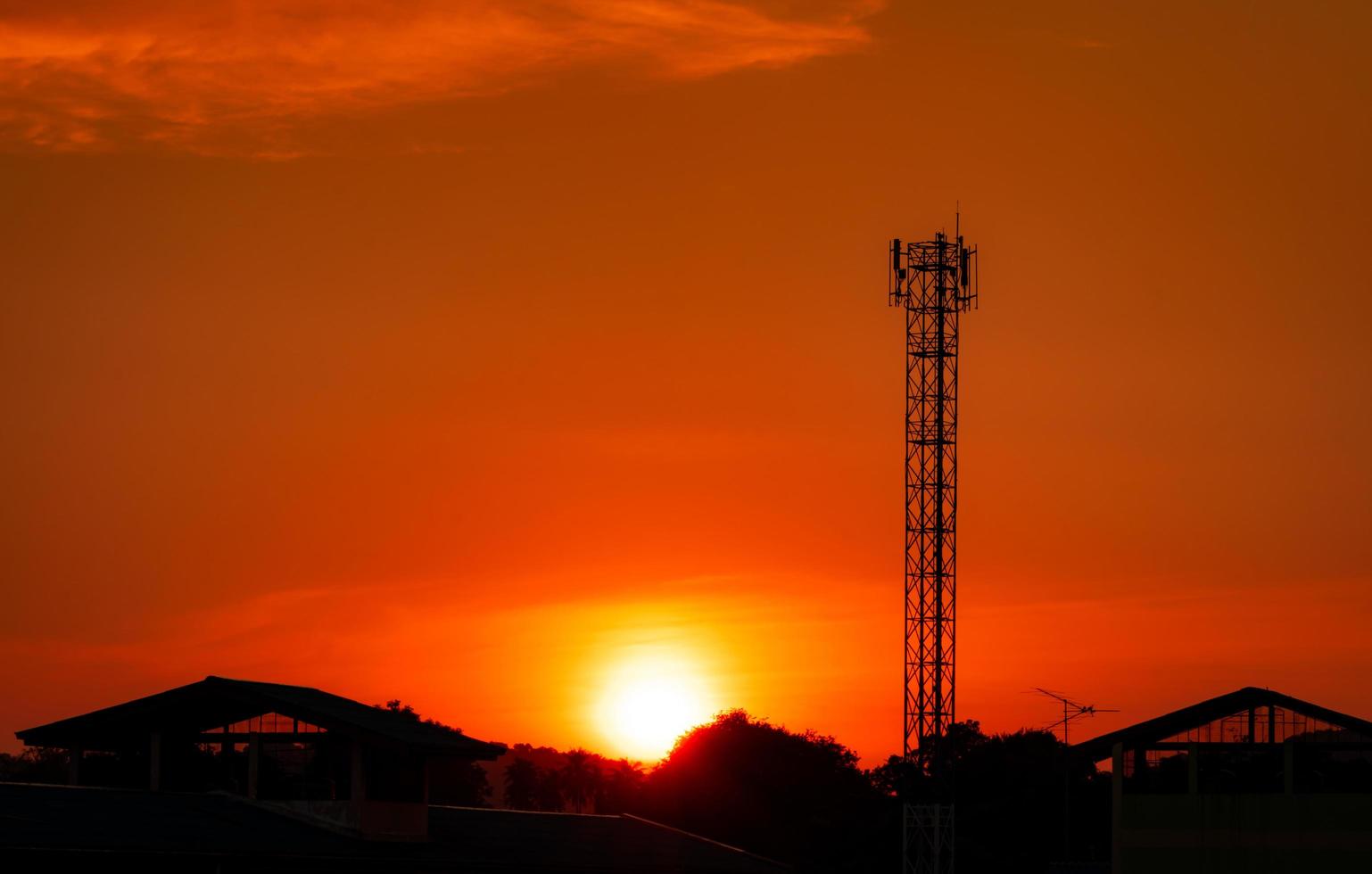 Telecommunication tower with red sunset sky and clouds. Radio and satellite pole. Communication technology. Telecommunication industry. Mobile or telecom 4g network. Silhouette rural house and forest. photo