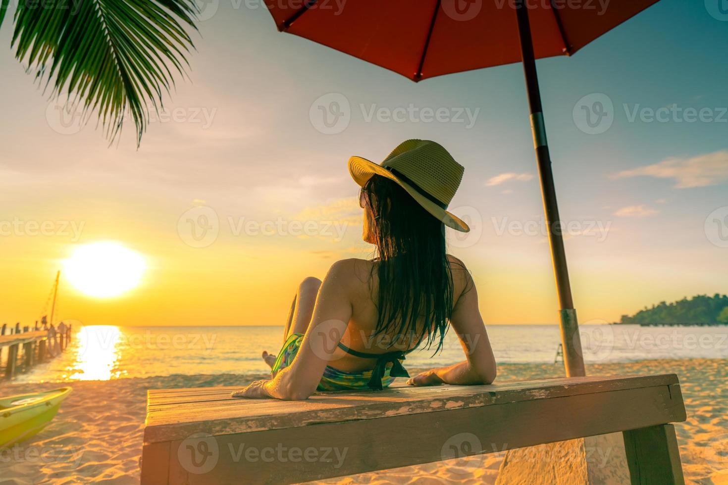 sexy, disfruta y relájate, la mujer usa bikini acostada y toma el sol en la tumbona en la playa de arena en la isla tropical paradisíaca bajo la sombrilla de playa al atardecer. vacaciones de verano. viajes de vacaciones vibras de verano. foto