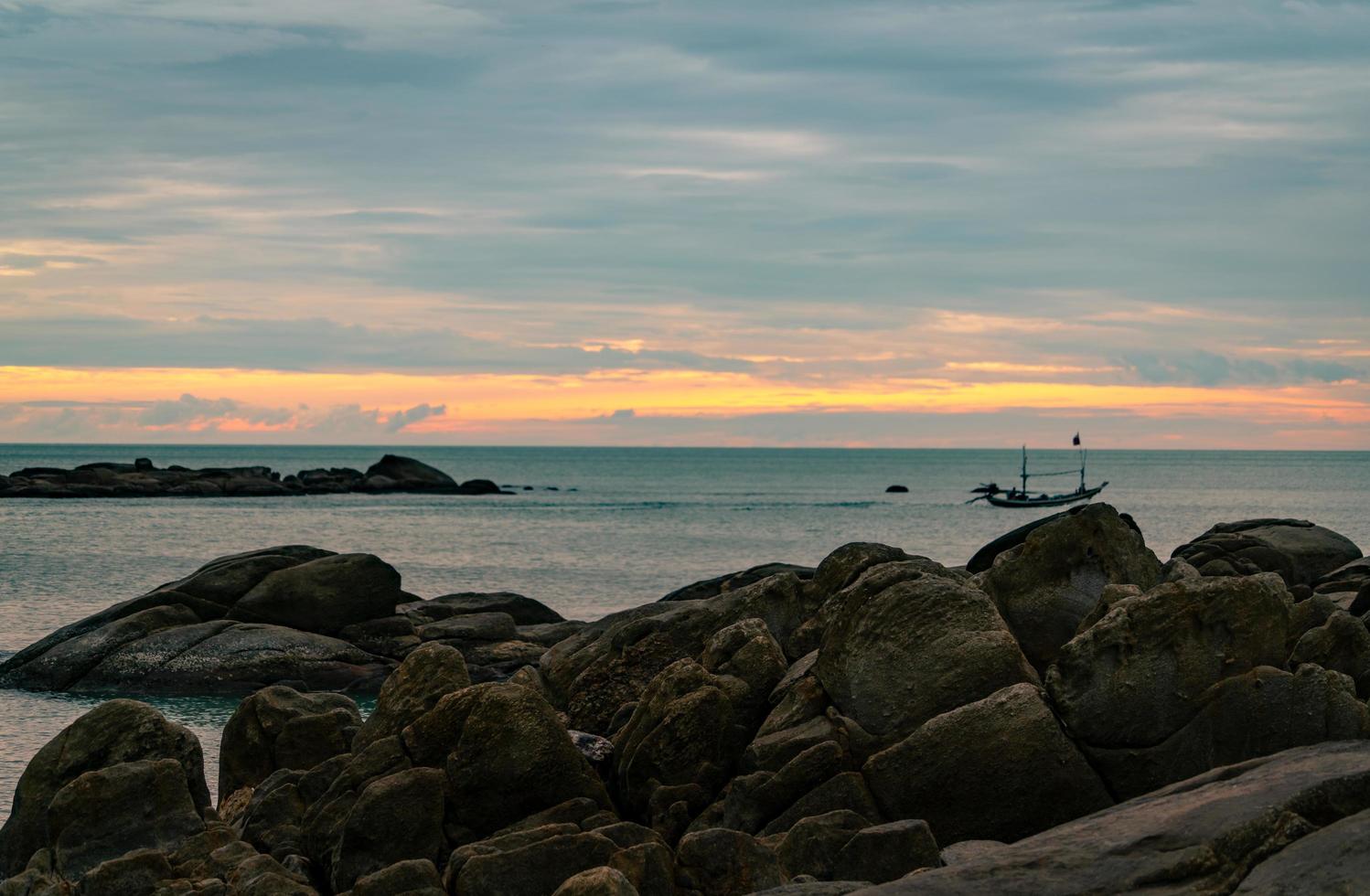 Beautiful stone beach in the morning with golden sunrise sky. Fisherman in long tail boat with folk fishing culture. Peaceful and tranquil scene. Calm sea in the morning. Seascape with skyline. photo