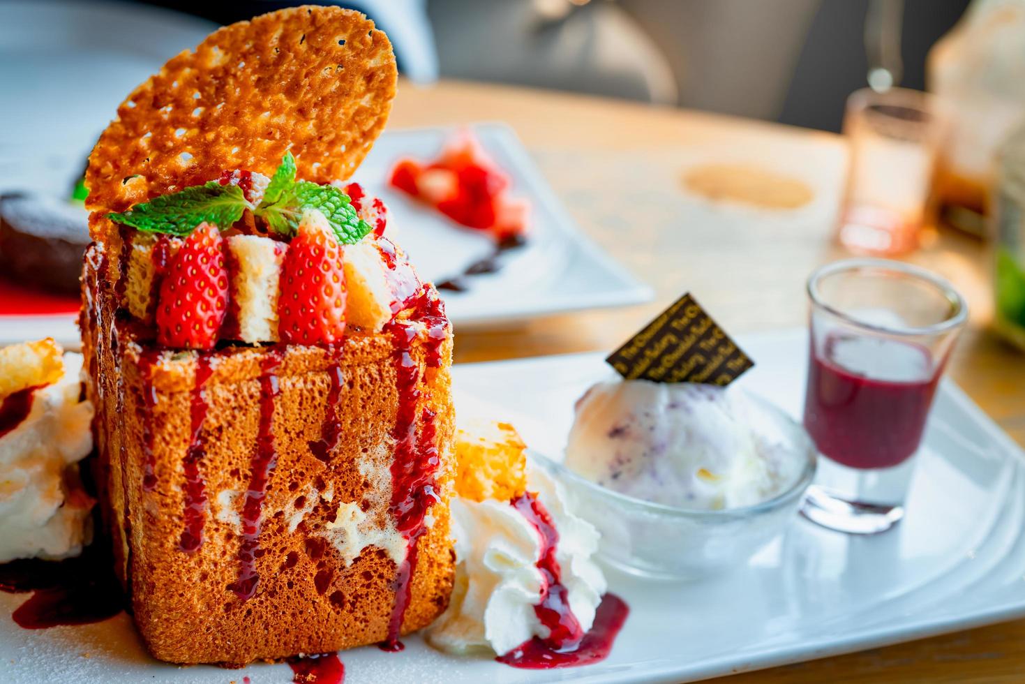 Honey toast topping with strawberries, a side of whipped cream, vanilla ice cream. Bread toast on white dish on blurred background of chocolate lava cake. Summer desserts. High calories food. photo