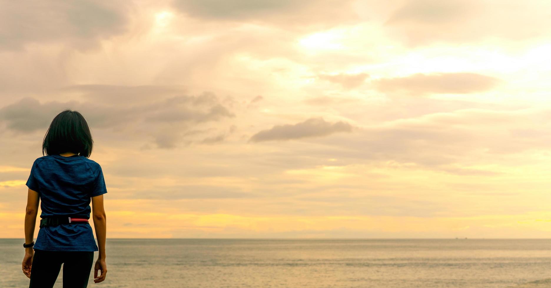 mujer asiática viendo el cielo del amanecer en la playa del mar. el corredor se relaja después de correr en la playa tropical. estilo de vida saludable. chica viaja sola en vacaciones de verano. vacaciones en la costa del océano. mujer feliz. foto