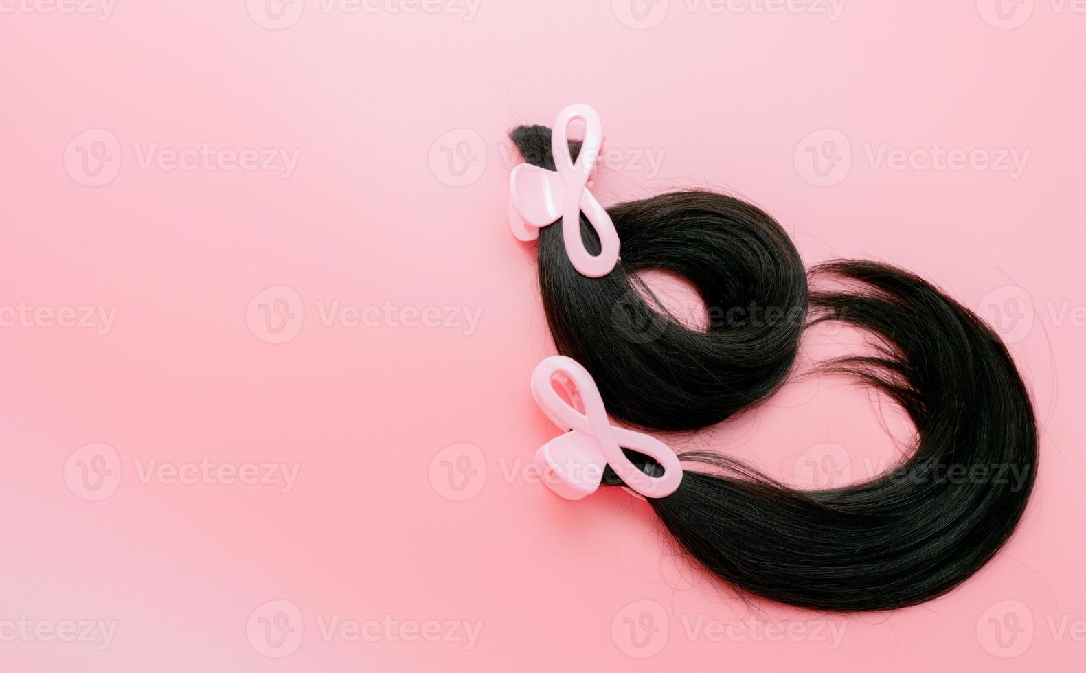 Hair donation for breast cancer person. Donate hair to wigs for breast cancer and leukemia patients. Donate to cancer charity. Long human hair with hair clip claw for donation on pink background. photo