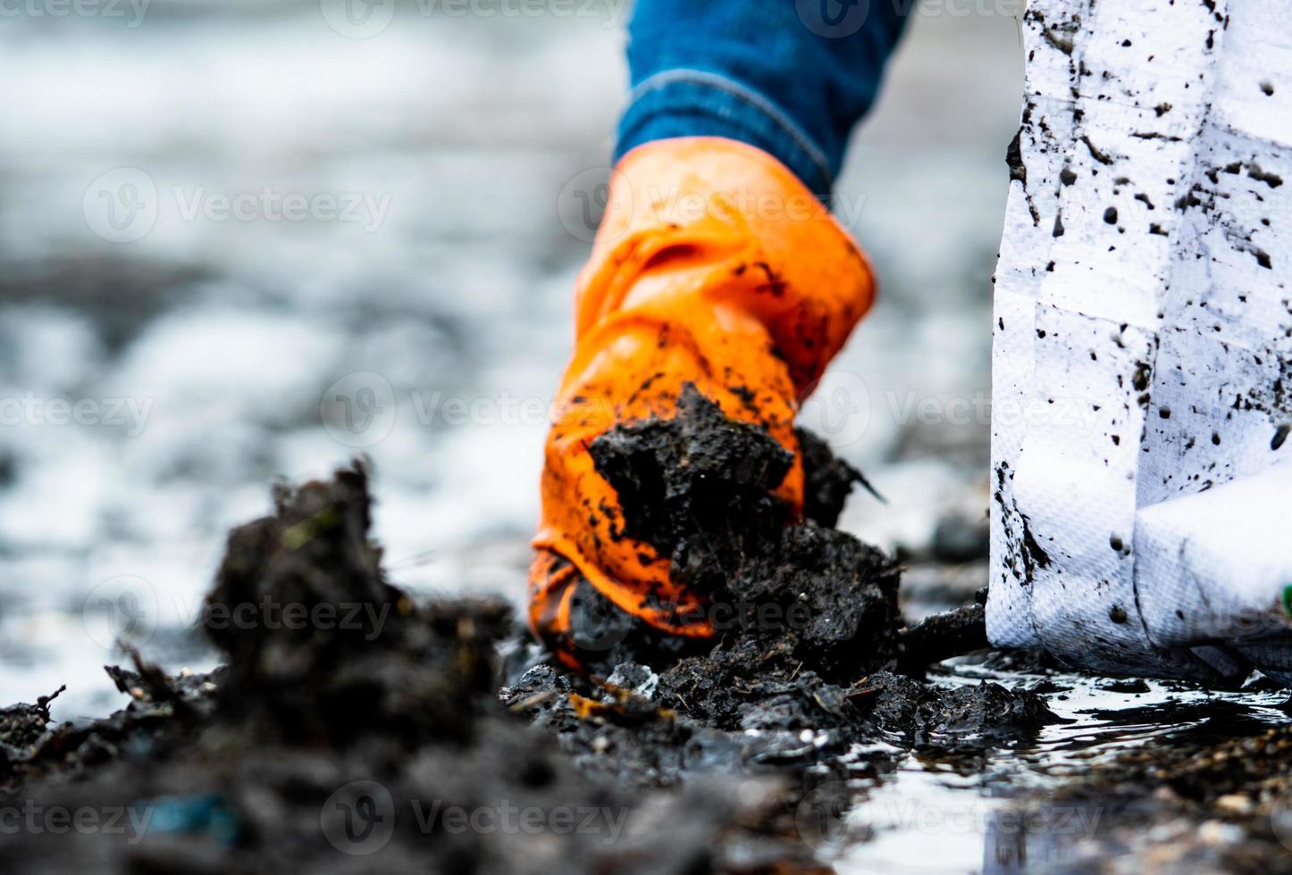 People wear orange gloves picking garbage up in to white bag. Closeup hand of adult volunteers collecting black garbage on the sea beach. Beach environment pollution. Tidying up rubbish on beach. photo