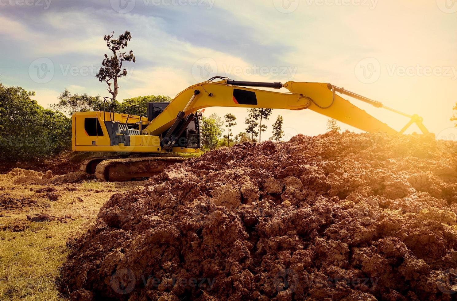 Backhoe working by digging soil at construction site. Excavator digging on earth. Earthmoving machine. Backhoe for rental business background. Pile of brown soil after digging by yellow excavator. photo