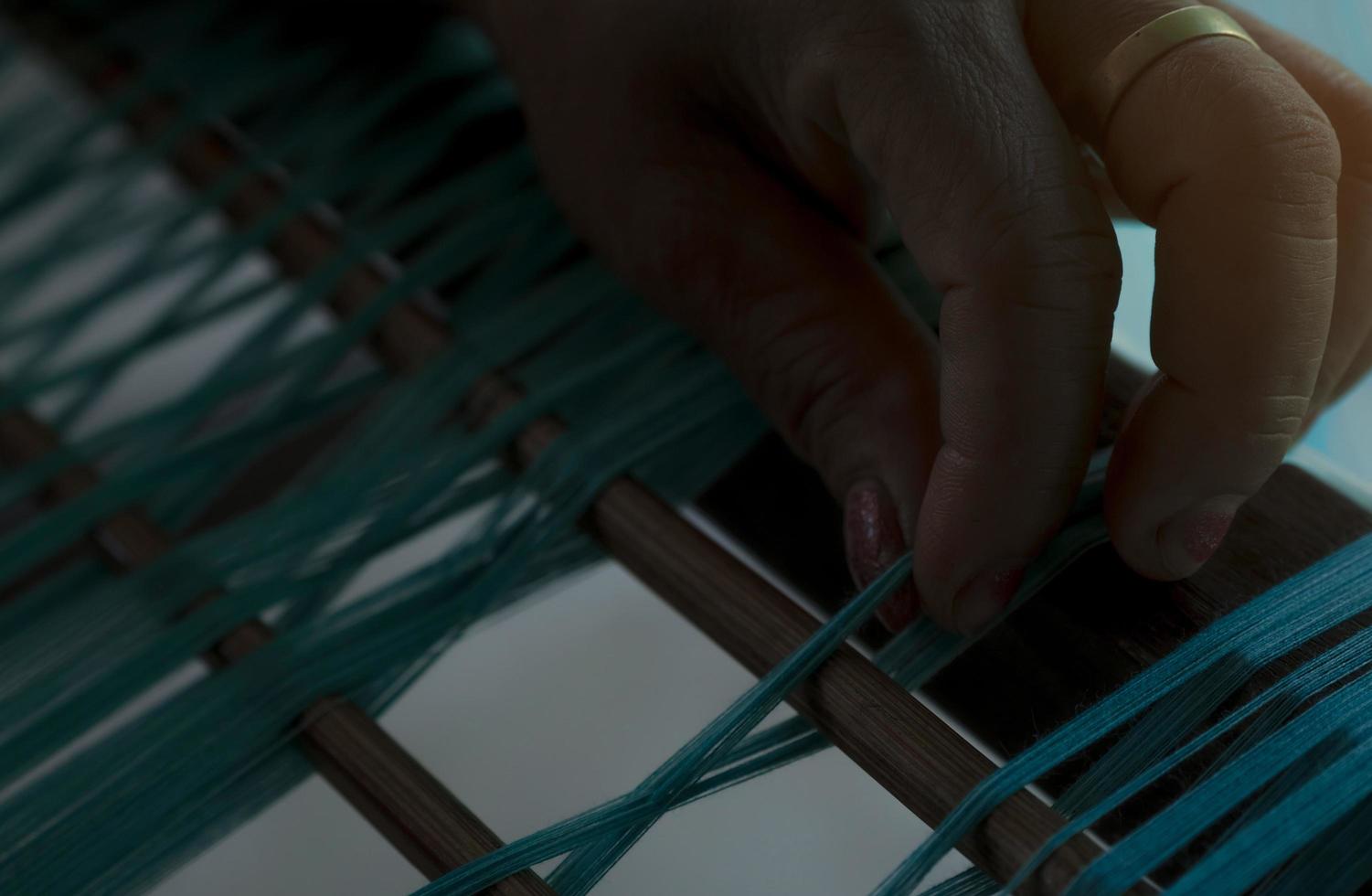 Selective focus on woman hand holding green cotton strands on weaving machine for weave handmade fabric. Textile weaving. Weaving using traditional hand weaving loom. Textile or cloth production. photo