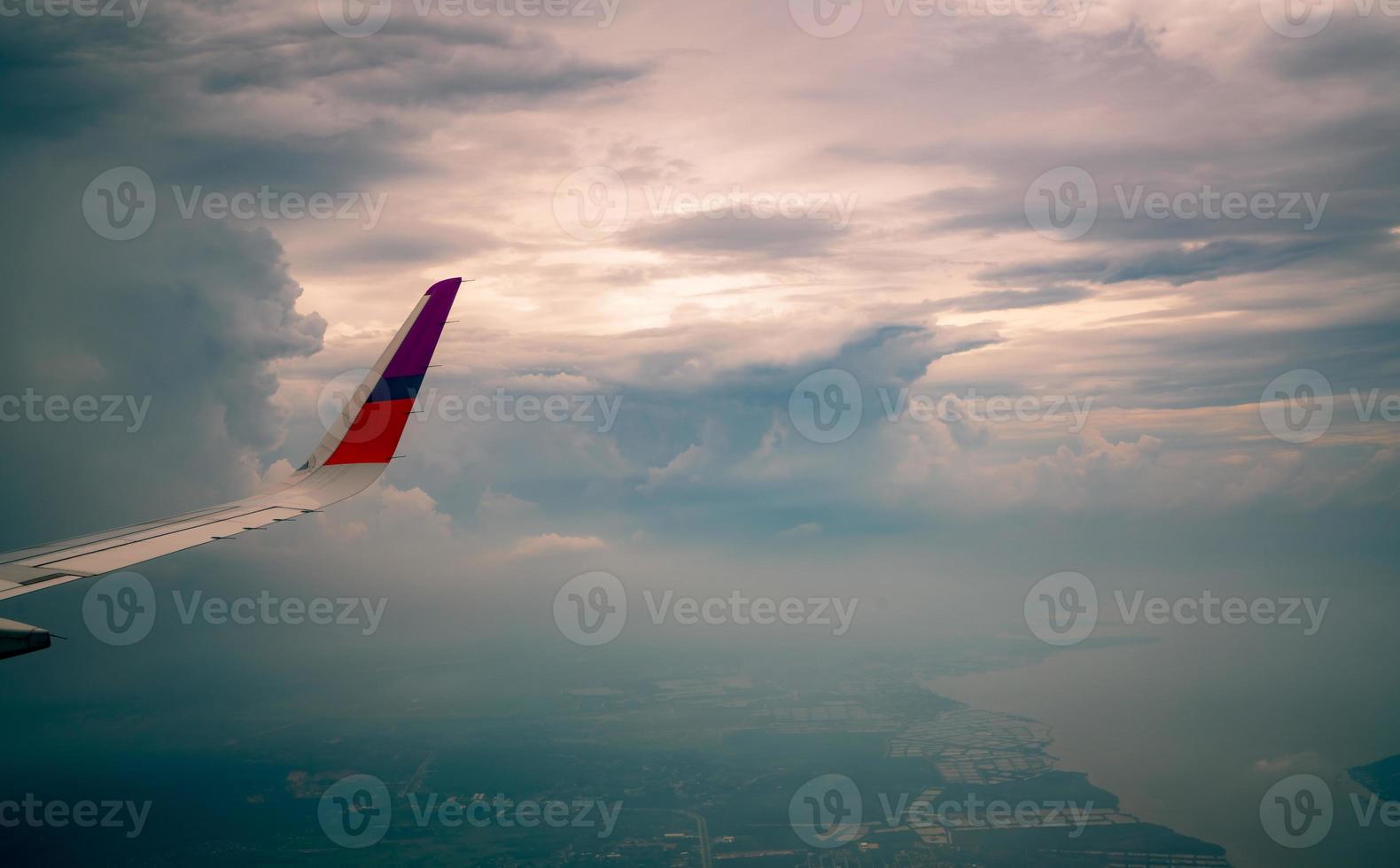 Wing of plane over the city. Airplane flying on blue sky. Scenic view from airplane window. Commercial airline flight in the morning with sunlight. Plane wing above clouds. Flight mechanics concept. photo