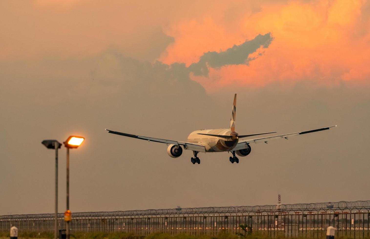 Commercial airline. Passenger plane landing at airport with beautiful sunset  sky and clouds. Arrival flight. Airplane flying over runway. Fence and taxiway lighting for safety flight in the evening. photo