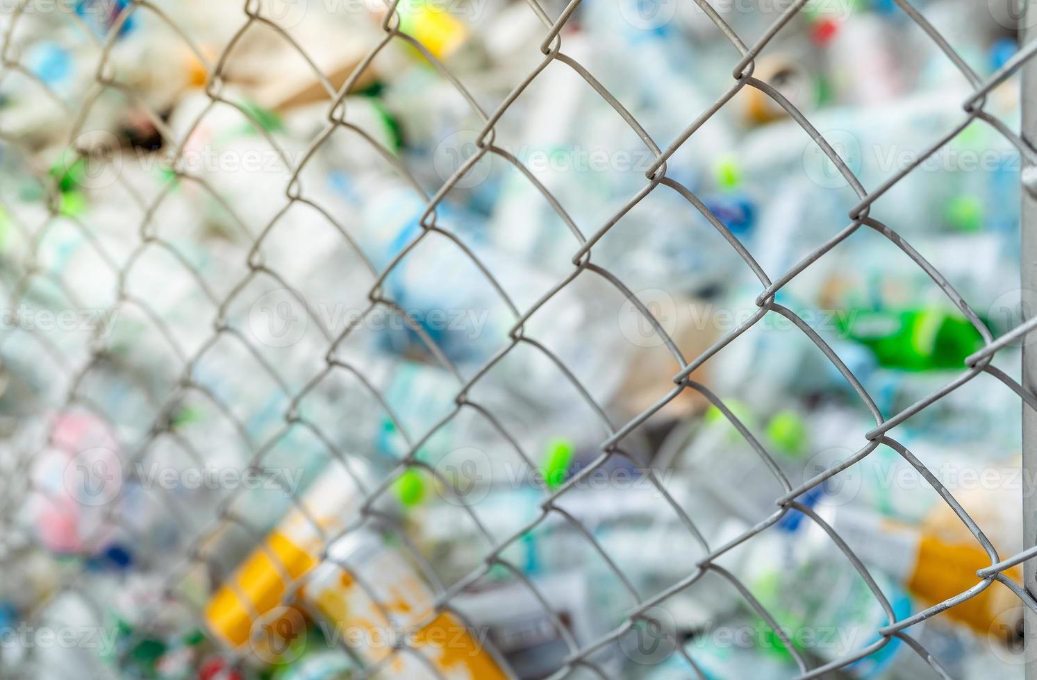 Blurred photo of pile of empty water plastic bottle in mesh fence recycle bin. Plastic bottle waste for recycle in recycling business. Plastic waste management. Reduce and reuse plastic. PET rubbish.