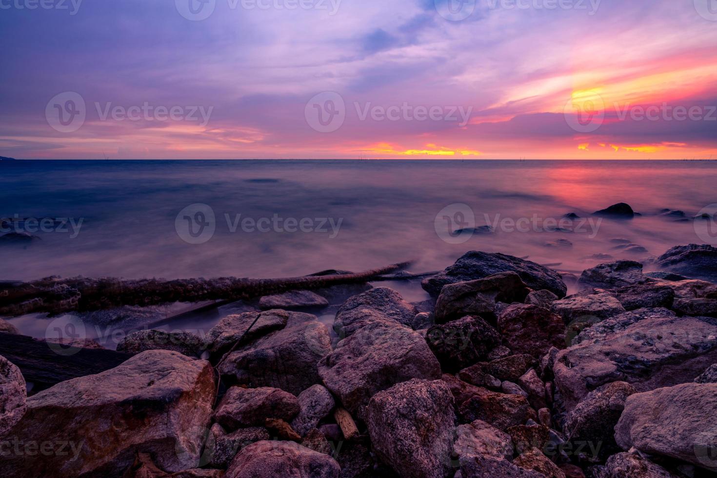 playa de piedra y mar tranquilo al atardecer con cielo púrpura al atardecer. mar tropical horizonte por la noche con cielo dorado, morado y rojo. marina. viajes de vacaciones de verano. costa de roca. belleza en la naturaleza del océano. foto