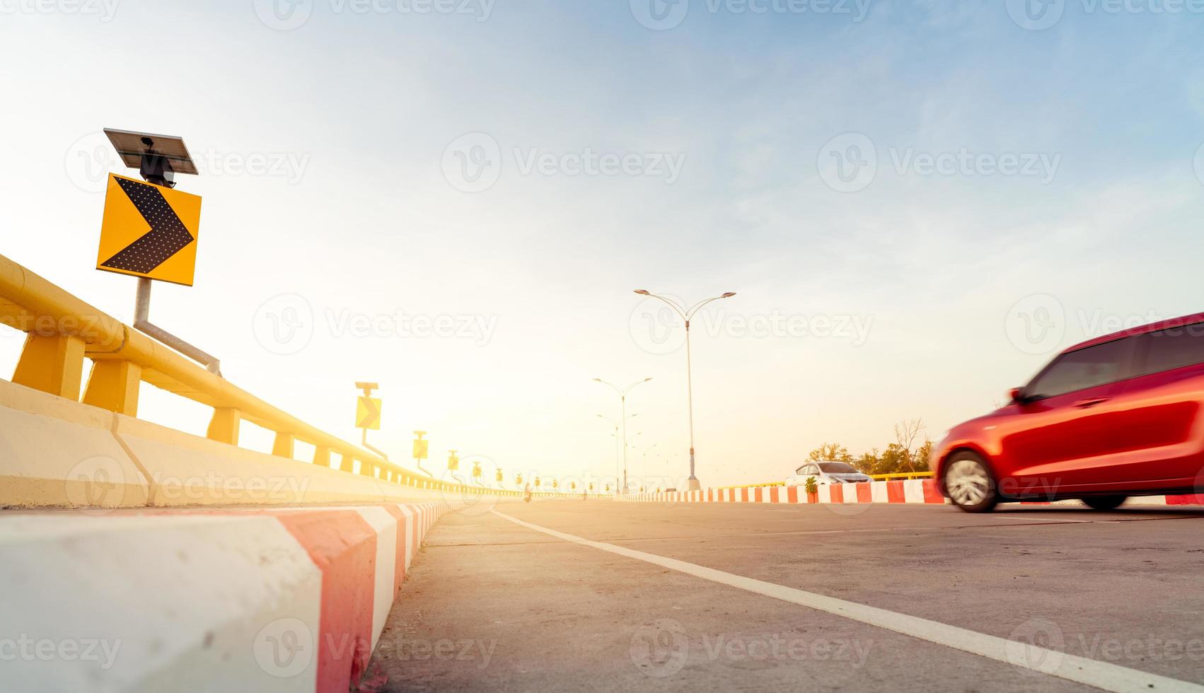Motion blur of red car driving on curve concrete road with traffic sign. Road trip on summer vacation. Car drive on the street. Summer travel by car. Solar panel energy on yellow curve traffic sign photo
