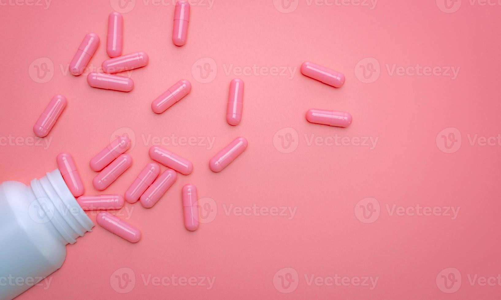 Pink capsule spread out of white plastic drug bottle. Capsule and pill bottle on pink background. Vitamins and supplements for healthy skin, collagen boost, and acne treatment concept. Online pharmacy photo