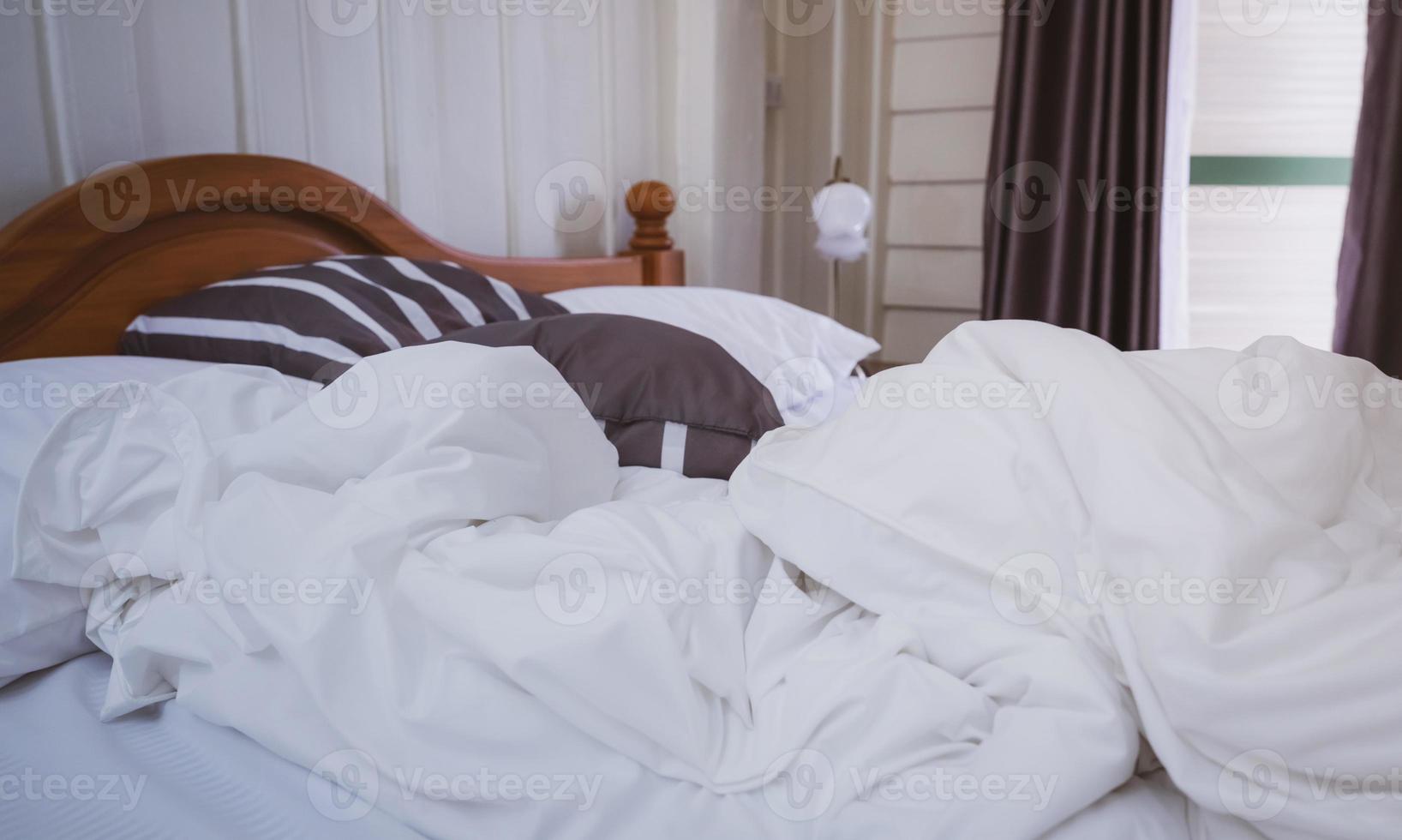 White comfort bed and soft pillow in vintage bedroom with window curtain and lamp. White linen blanket in vintage bedroom. Messy white blanket. Comfortable bed with soft white duvet. Bedroom interior. photo