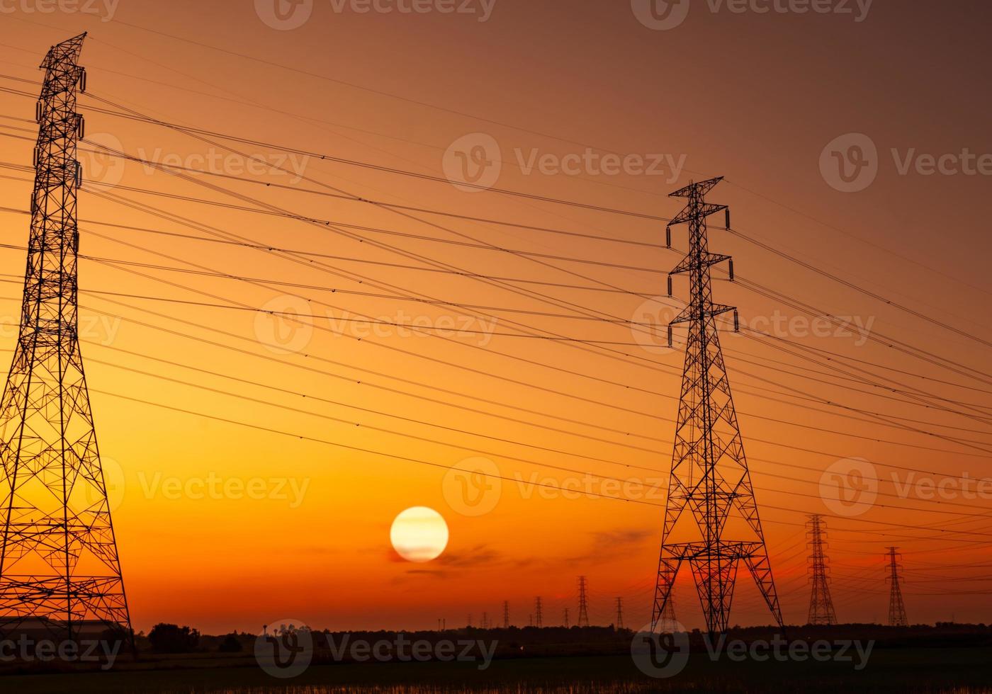 pilón eléctrico de alto voltaje y cable eléctrico con cielo al atardecer. postes de electricidad concepto de potencia y energía. torre de red de alto voltaje con cable de alambre. hermoso gran sol al atardecer con cielo rojo-naranja. foto