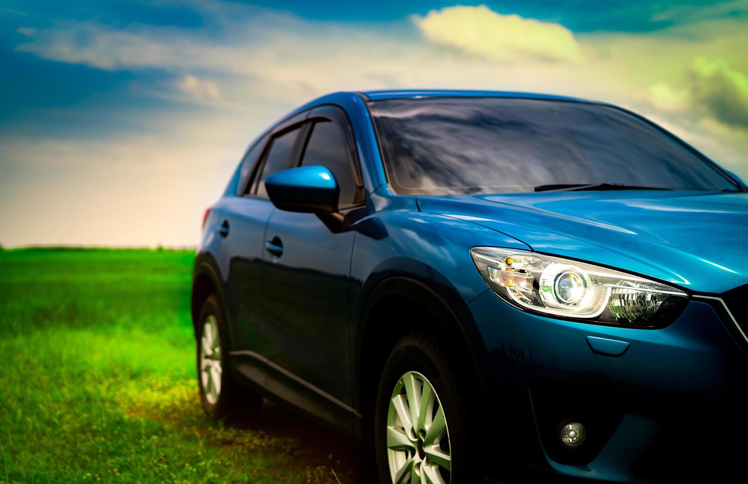 vista frontal de un lujoso camión suv compacto azul con diseño deportivo y moderno estacionado en un campo de hierba verde con cielo azul y nubes blancas. automóvil híbrido y automotriz. viaje por carretera y conducción de automóviles para viajar. foto